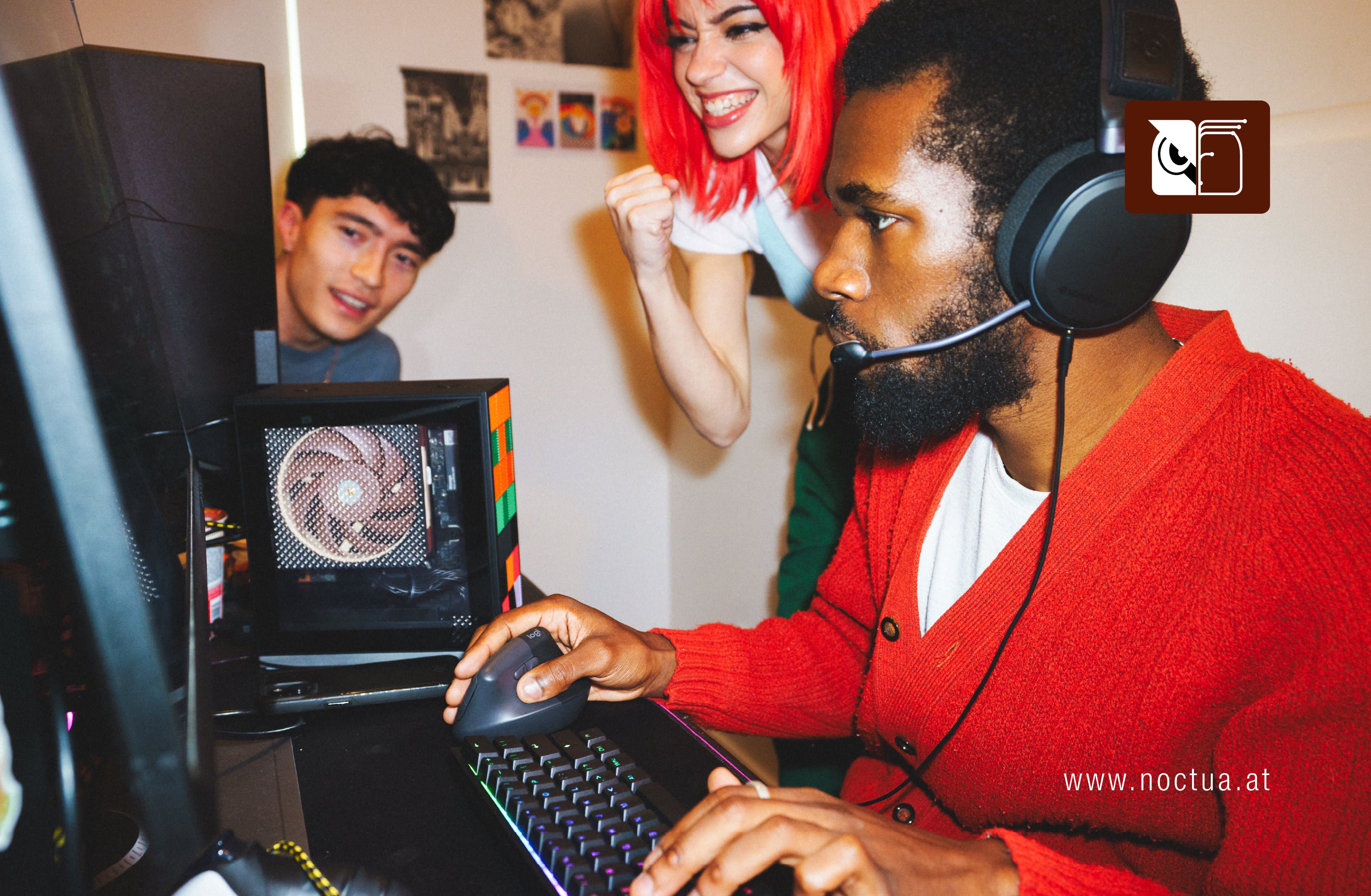 A gamer wearing a headset playing on a Framework PC with a visible Noctua fan, cheered on by friends, showing a compact gaming setup.