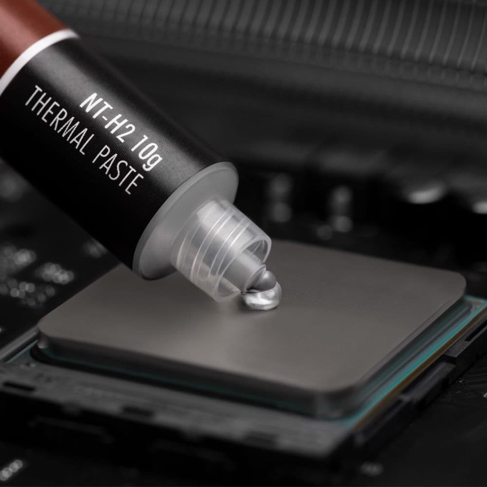A close-up shot of Noctua NT-H2 10g thermal paste being applied to the center of a CPU's heat spreader.
