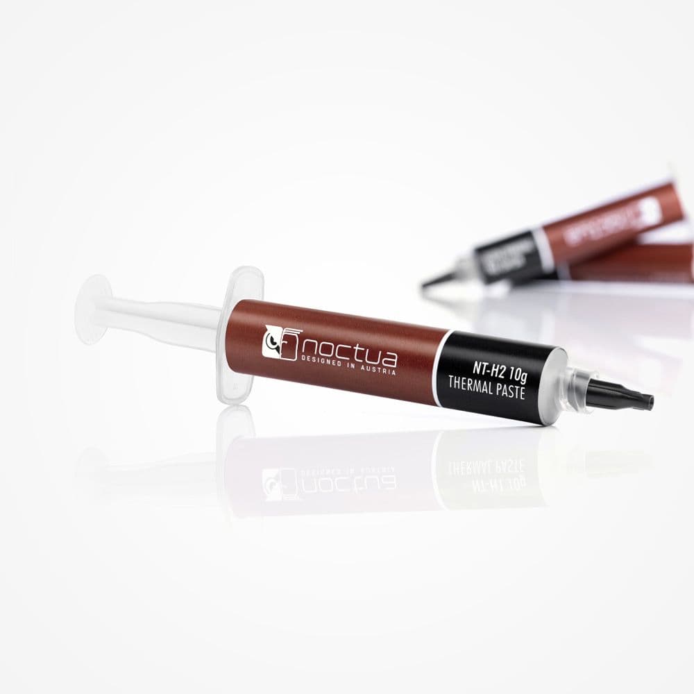 An angled shot of a syringe of Noctua NT-H2 10g thermal paste on a reflective white surface, with two syringes in the background.